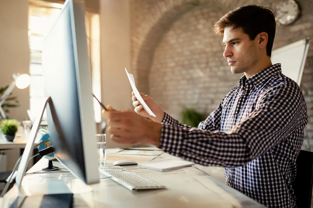 Employee doing manual work with documents and spreadsheets, illustrating the inefficiency of non-automated processes